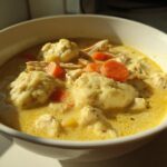 Close-up of a white bowl filled with creamy gluten free chicken and dumplings, featuring shredded chicken and bright orange carrots.