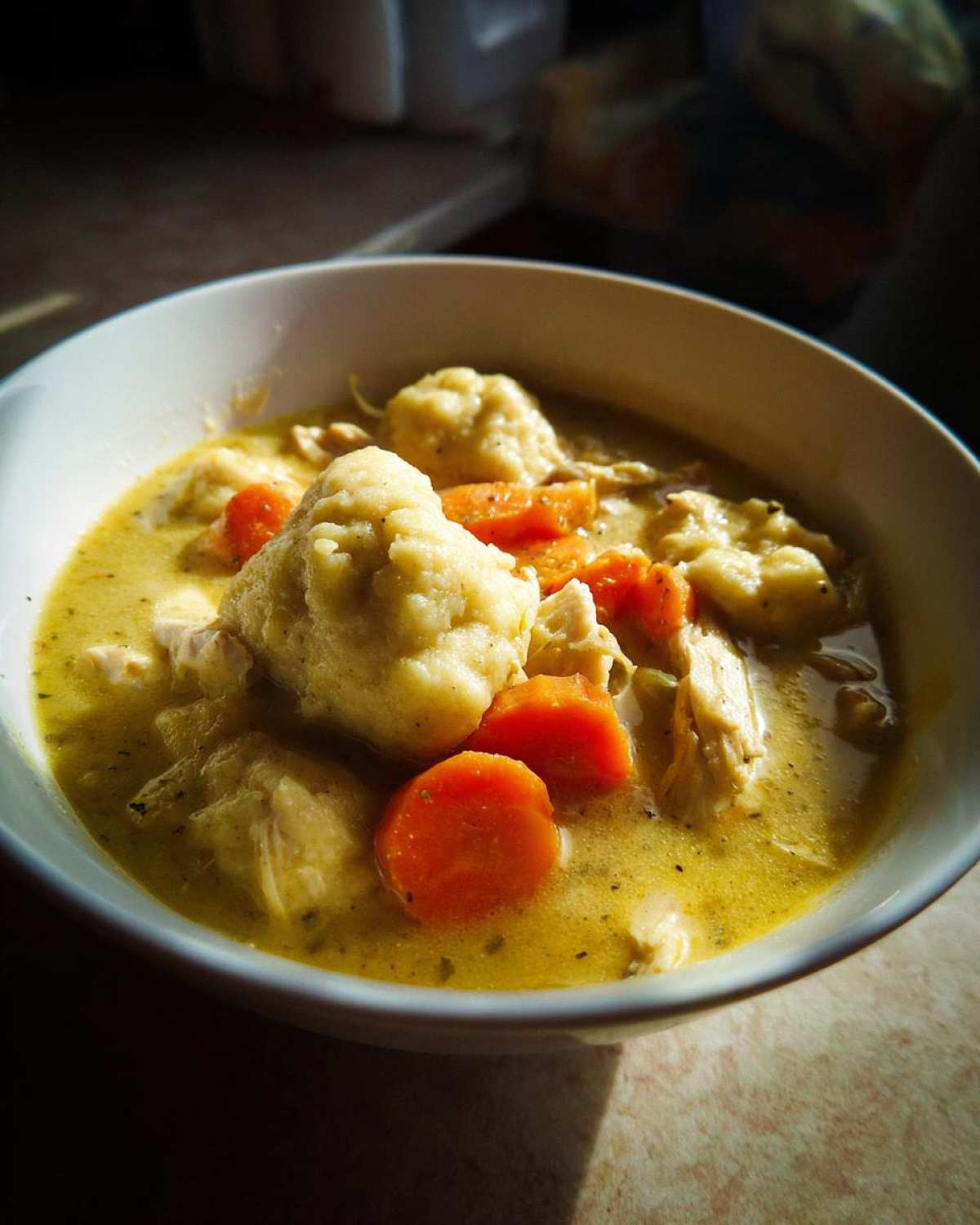 Close-up of a creamy bowl of gluten free chicken and dumplings, featuring fluffy dumplings and bright orange carrot slices.