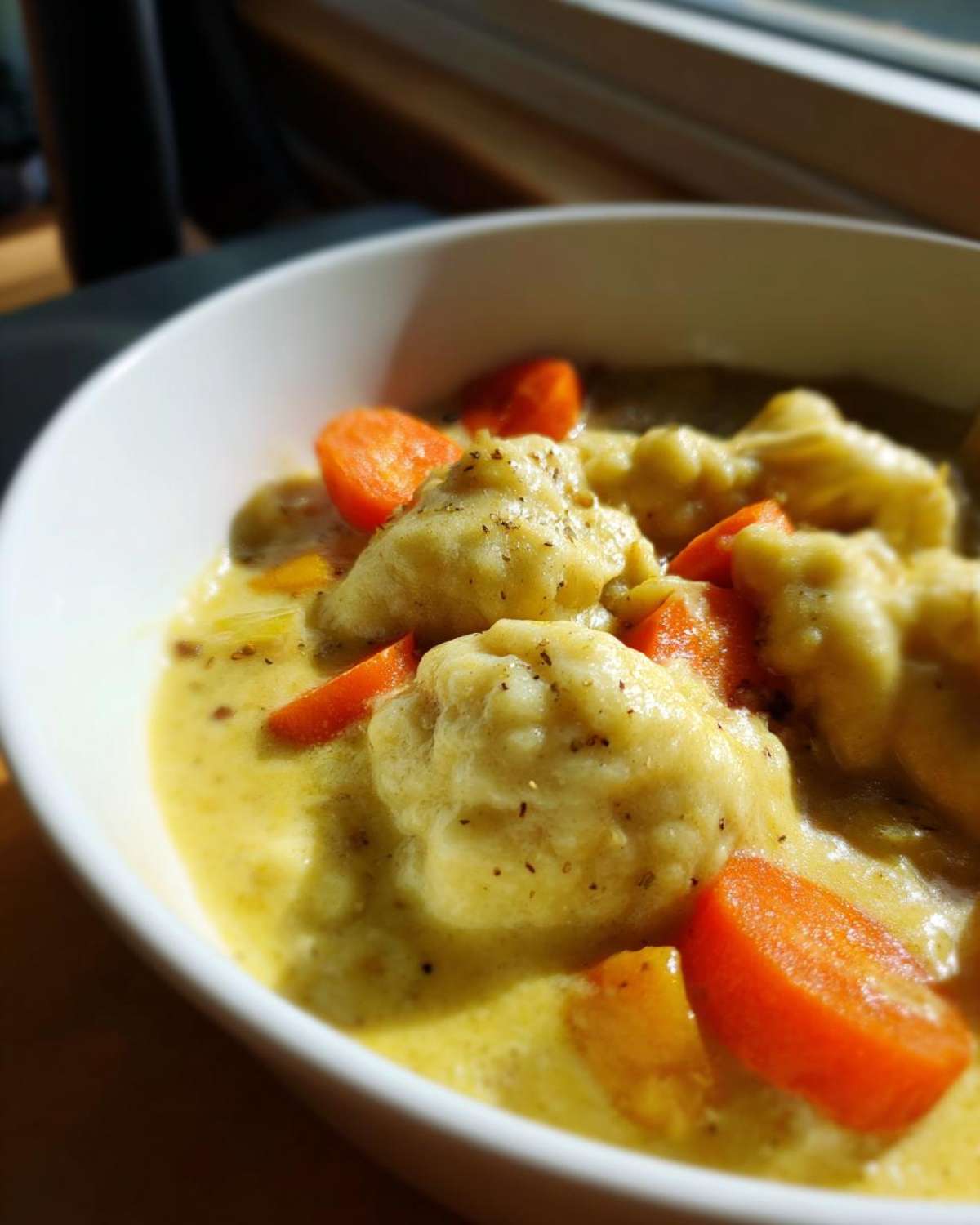 Close-up of fluffy dumplings and bright orange carrots in a creamy sauce from a bowl of gluten free chicken and dumplings.