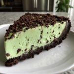 A close-up slice of bright green grasshopper pie with chocolate chips in the filling and a dark chocolate crust.