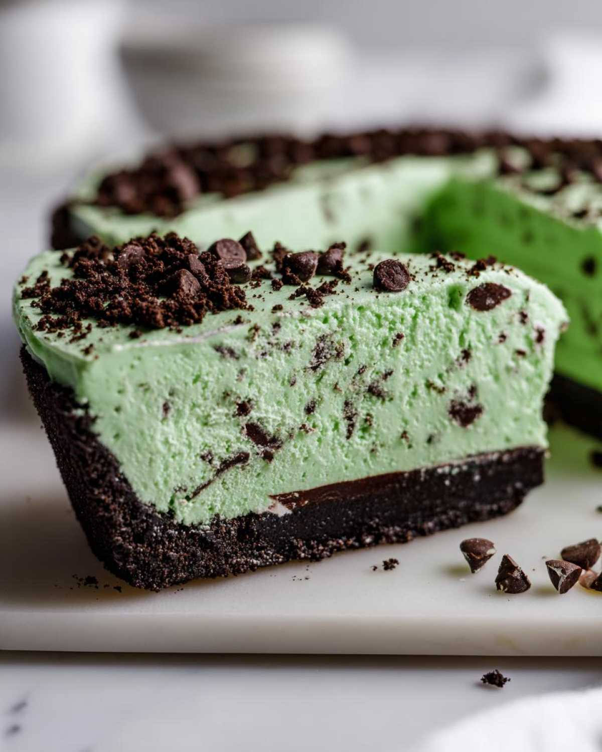 A close-up slice of bright green grasshopper pie with a dark chocolate crust, topped with chocolate chips.