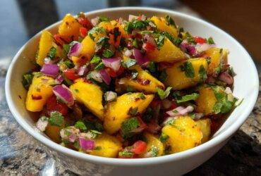 Close-up of vibrant peach salsa chunks mixed with red onion, cilantro, and peppers in a white bowl.
