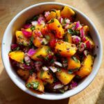 Close-up of vibrant grilled peach salsa featuring chunks of orange peach, red onion, and cilantro in a white bowl.