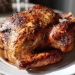 A beautifully roasted turkey with dark, herb-crusted, crispy skin resting on a white platter.