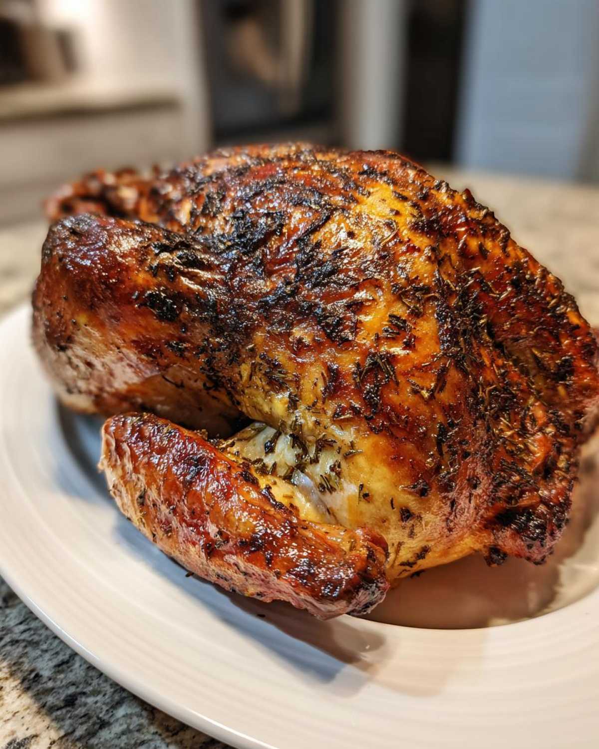 A perfectly roasted whole turkey seasoned with herbs, featuring dark, crispy skin, resting on a white platter.