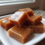 Close-up of several chewy, square pieces of homemade caramel stacked on a small white dish.