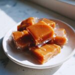 A stack of individually wrapped, chewy homemade caramel squares sitting on a small white plate.