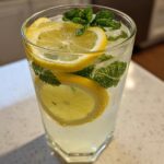 Close-up of a tall glass filled with homemade lemonade, ice, lemon slices, and fresh mint leaves.