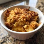 A close-up shot of a warm, freshly baked apple crumble served in a white ramekin, showing the crunchy topping.