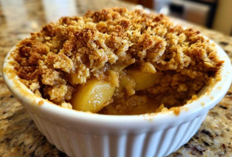 A close-up view of a single-serving apple crumble baked in a white ramekin, showing golden topping and soft cooked apples.