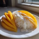 A serving of vibrant mango sticky rice, featuring sliced yellow mango and sticky rice drizzled with coconut cream.