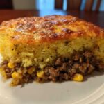 A thick slice of Mexican cornbread casserole showing a golden, baked top layer over a savory ground beef and corn filling.