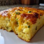 Close-up of a moist slice of Mexican cornbread topped with melted cheddar cheese and green jalapeño pieces.