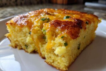 Close-up of a moist slice of Mexican cornbread topped with melted cheddar cheese and green jalapeño pieces.