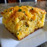 A close-up, tasty shot of a slice of Mexican cornbread topped with melted cheddar cheese and green onions.