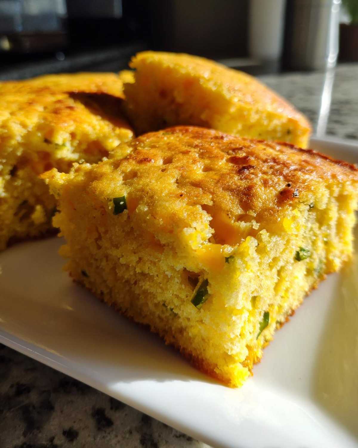 Close-up of moist, golden Mexican cornbread squares with visible green jalapeño pieces, served on a white plate.