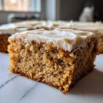 Close-up of a moist slice of applesauce cake topped with thick, light brown frosting.