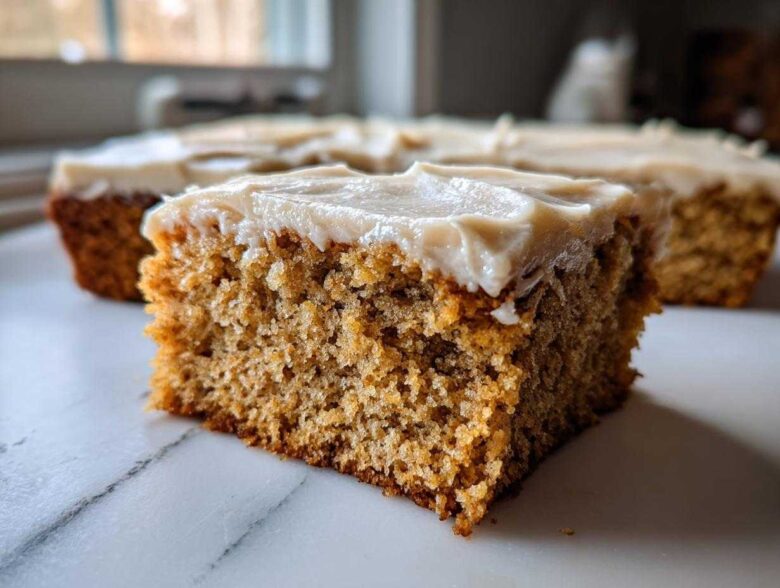 Close-up of a moist slice of applesauce cake topped with thick, light brown frosting.