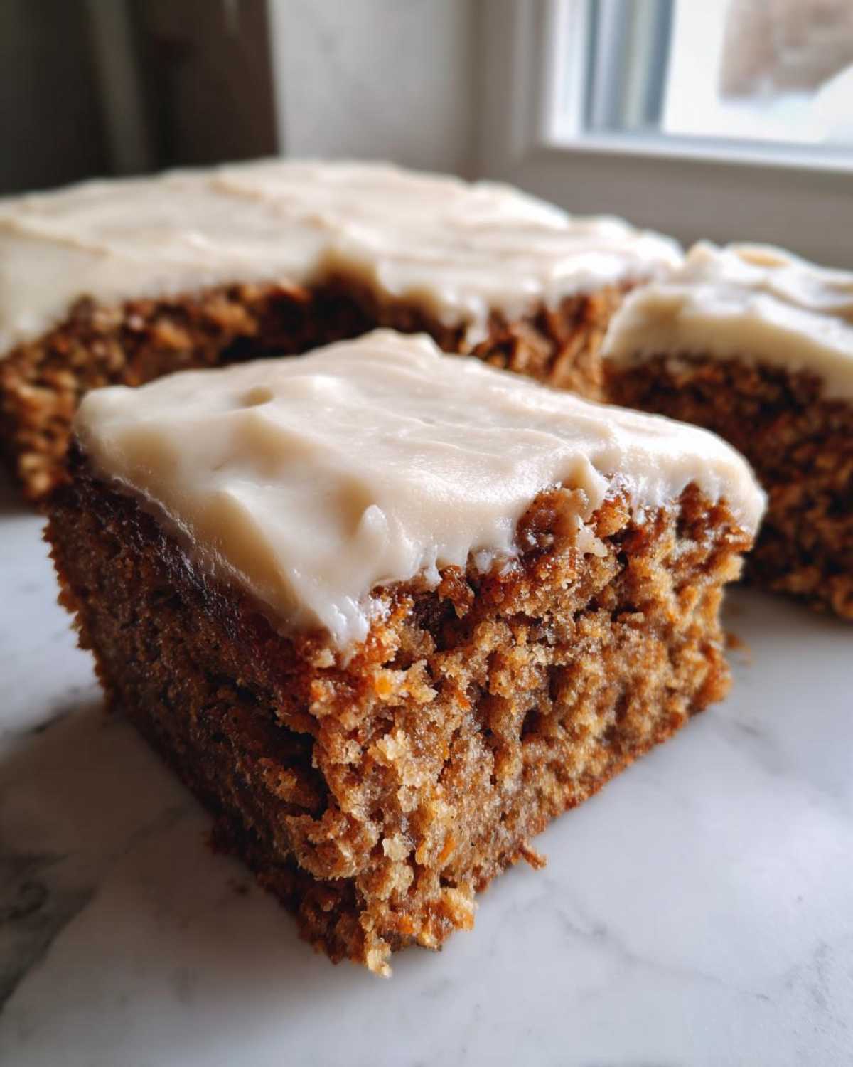 Close-up of a moist slice of applesauce cake topped with thick cream cheese frosting.