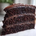 Close-up of a moist, dark slice of three-layer chocolate cake recipe with rich frosting.
