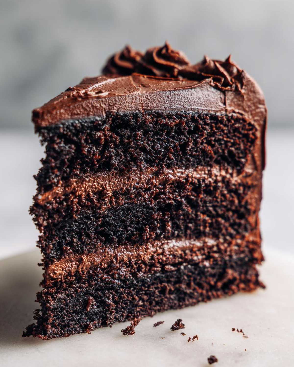 Close-up of a moist, dark slice of chocolate cake recipe with three layers and rich chocolate frosting.