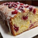 Close-up of a moist cranberry orange bread loaf topped with a white glaze and fresh cranberries.