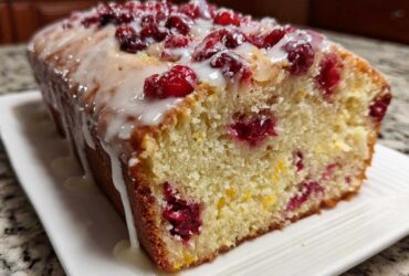 Close-up of a moist cranberry orange bread loaf topped with a white glaze and fresh cranberries.