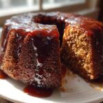 A moist, dark brown rum cake with a thick, glossy rum glaze dripping down the sides, sitting on a white plate.