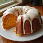 A slice removed from a moist sweet potato pound cake topped with dripping vanilla glaze on a white plate.