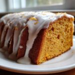 A thick slice of moist sweet potato pound cake drizzled with white glaze and orange zest.