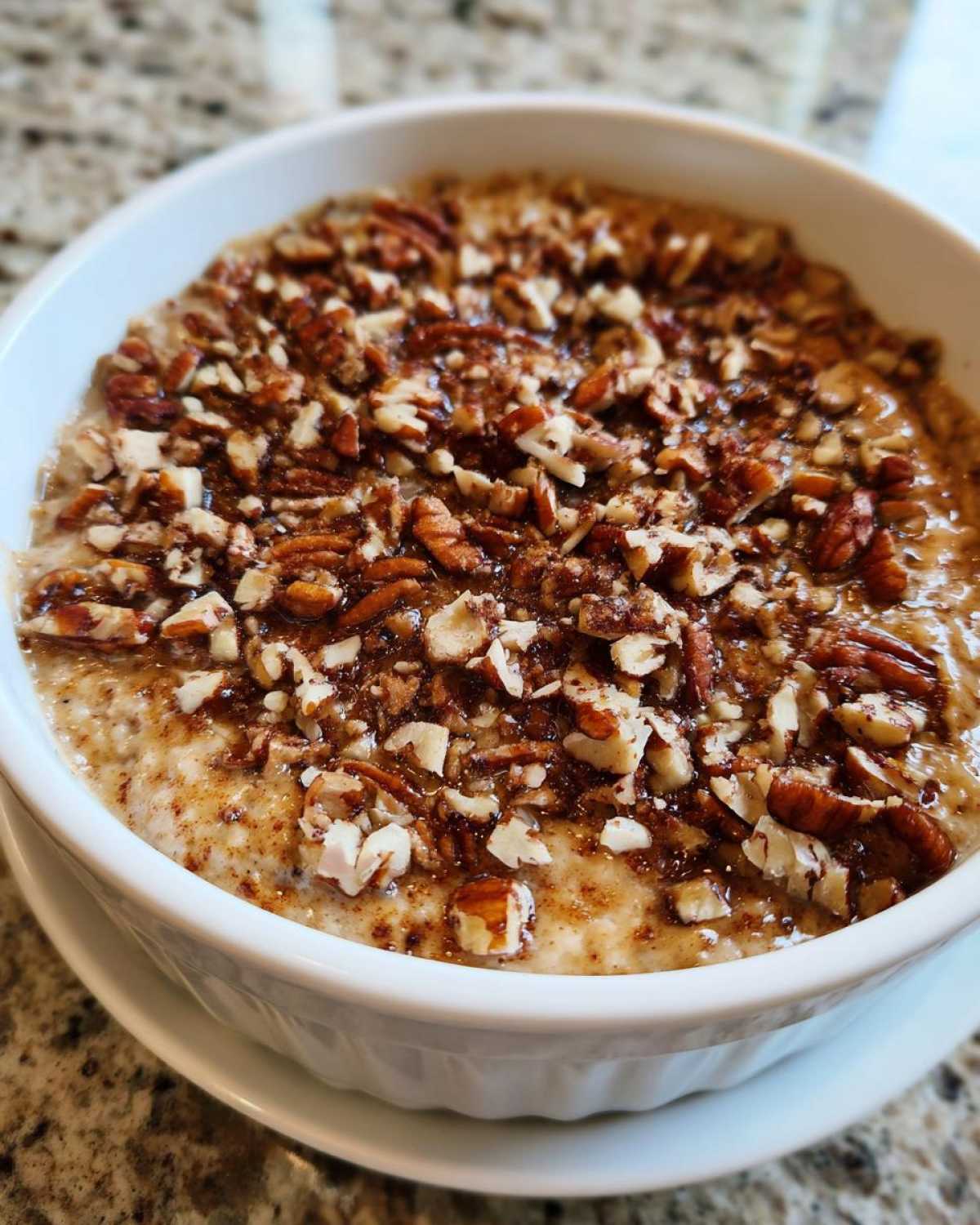 A close-up of a white bowl filled with creamy pecan pie dip, generously topped with chopped pecans and a sweet glaze.