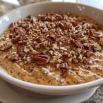 Close-up of a creamy, orange-hued no-bake pecan pie dip topped generously with chopped pecans.