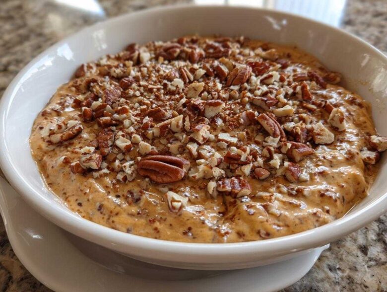 Close-up of a creamy, orange-hued no-bake pecan pie dip topped generously with chopped pecans.