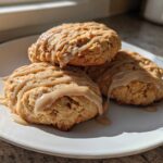 Three freshly baked apple pie cookies drizzled with a light brown glaze, stacked on a white plate.