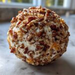 A close-up, featured image of a perfectly formed cheese ball recipe coated entirely in chopped pecans.