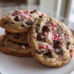 A stack of freshly baked, chewy peppermint chocolate chip cookies topped with crushed candy canes.