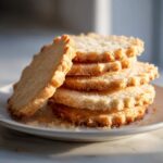 A stack of five golden brown, perfectly shaped sugar cookie rounds with crimped edges, resting on a white plate.