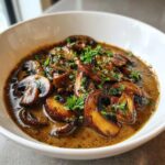 Close-up of rich, brown mushroom sauce filled with sautéed mushroom slices and topped with fresh parsley.