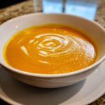 Close-up of vibrant orange roasted butternut squash soup garnished with a swirl of cream.