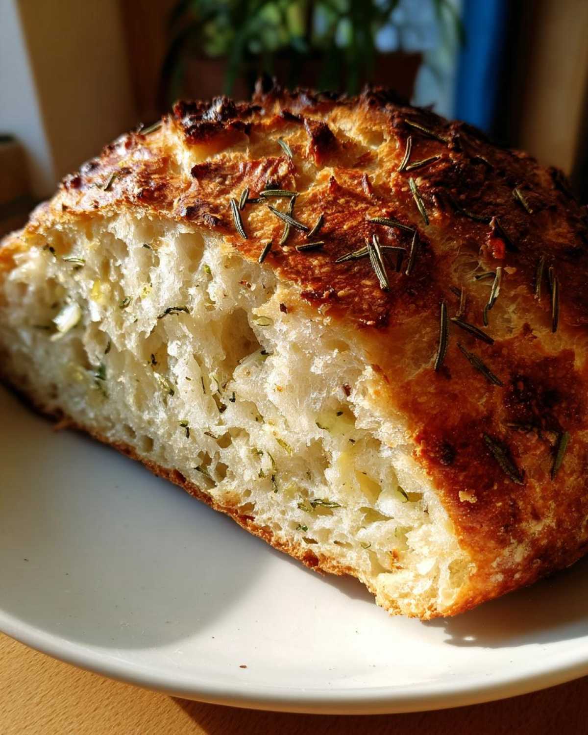 Close-up of a slice of homemade artisan bread showing an open, airy crumb studded with herbs.