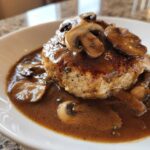 Close-up of a perfectly cooked Salisbury steak smothered in rich mushroom gravy and topped with sliced mushrooms.
