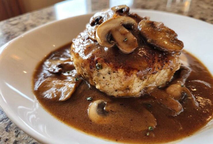 Close-up of a perfectly cooked Salisbury steak smothered in rich mushroom gravy and topped with sliced mushrooms.