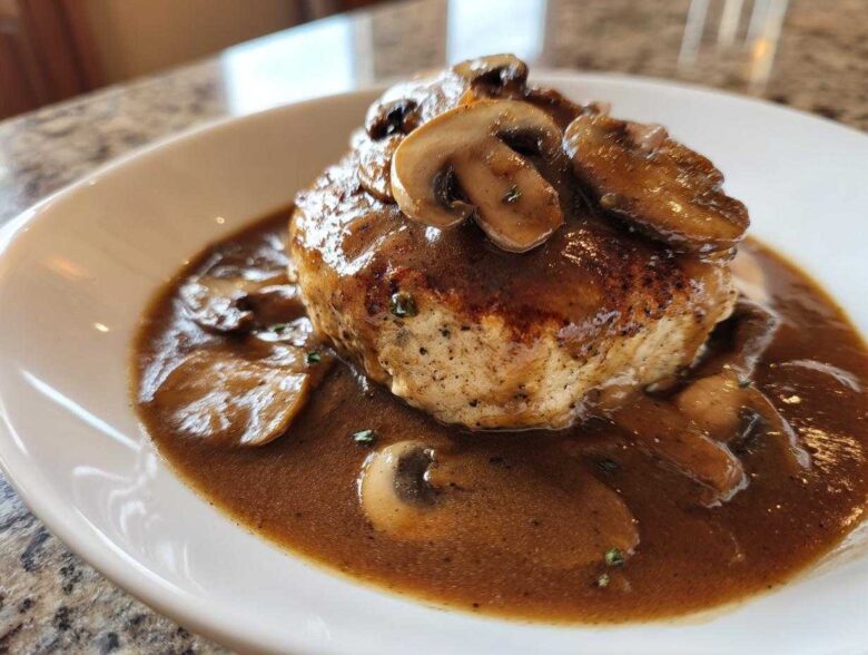 Close-up of a perfectly cooked Salisbury steak smothered in rich mushroom gravy and topped with sliced mushrooms.