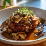 Close-up of a perfectly cooked salisbury steak smothered in rich mushroom gravy and garnished with fresh rosemary.