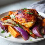 A piece of juicy harissa chicken served over roasted carrots and purple onions, garnished with parsley.
