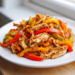 A close-up of shredded chicken mixed with vibrant red, yellow, and green bell pepper strips for crockpot chicken fajitas.