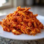 A close-up of a mound of saucy, shredded chicken tinga piled high on a white plate.