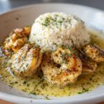Close-up of seasoned shrimp in buttery sauce next to garlic parmesan rice, part of a chicken scampi dish.