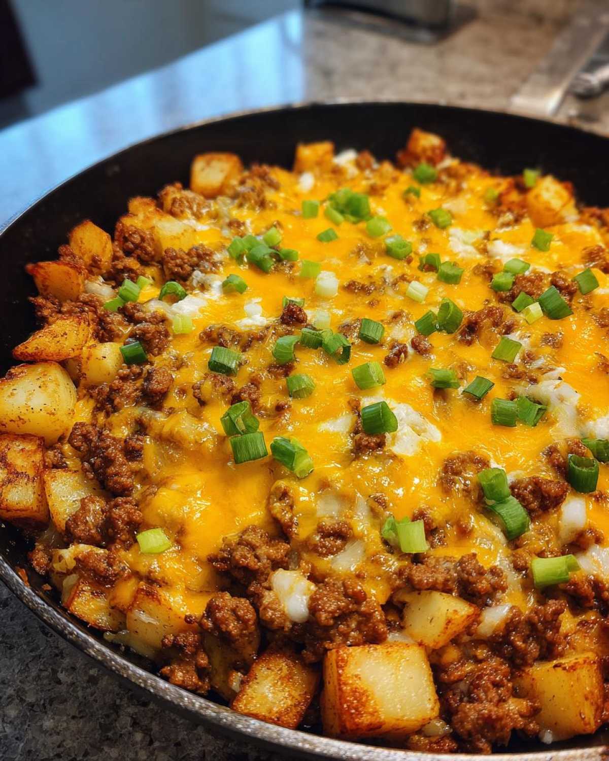 Close-up of Cheesy Taco Potatoes in a skillet, featuring seasoned ground meat, golden potatoes, melted cheddar cheese, and chopped green onions.
