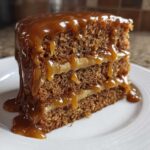 Close-up of a moist slice of 3 layer caramel cake dripping with thick, glossy caramel sauce.